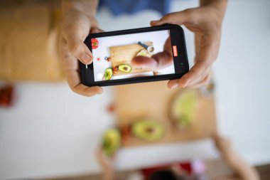 Akıllı telefonlu bir kadın, avokado kesen küçük bir kızı kaydediyor.