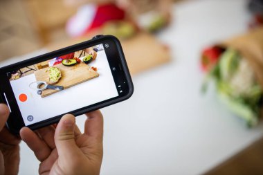 Akıllı telefonlu bir erkek el, küçük bir kızın avokado kestiğini kaydediyor.