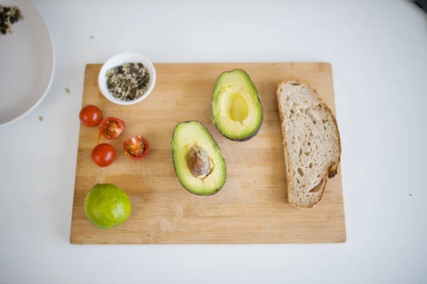 Sliced bread, avocado cut in half, seeds, and tomatoes on cutting board — Stock Photo, Image