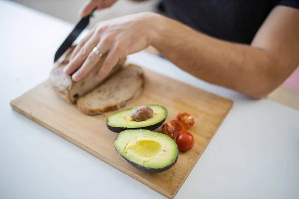 Male hand slicing bread and avocados on a cutting board