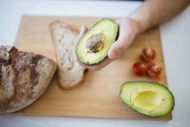 Kesme tahtasının üzerinde kesilmiş avokado tutan bir erkek.