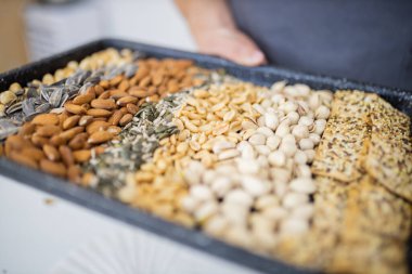 Erkek el siyah bir tepsi fındık ve tohum tutuyor.