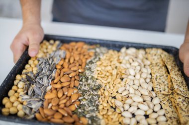 Erkek el siyah bir tepsi fındık ve tohum tutuyor.