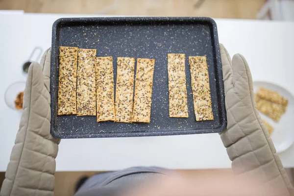 Handschuh in der Hand hält ein schwarzes Tablett mit schwedischem Knäckebrot — Stockfoto