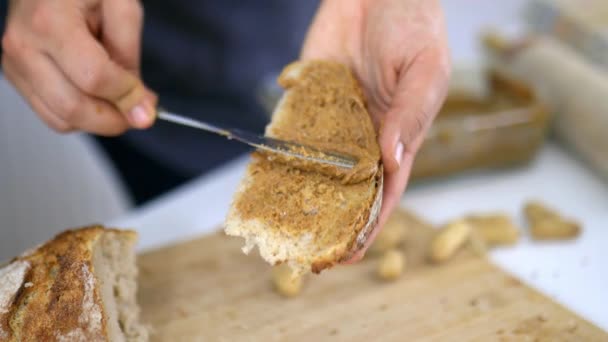 Mãos femininas espalhando manteiga de amendoim em uma fatia de pão — Vídeo de Stock
