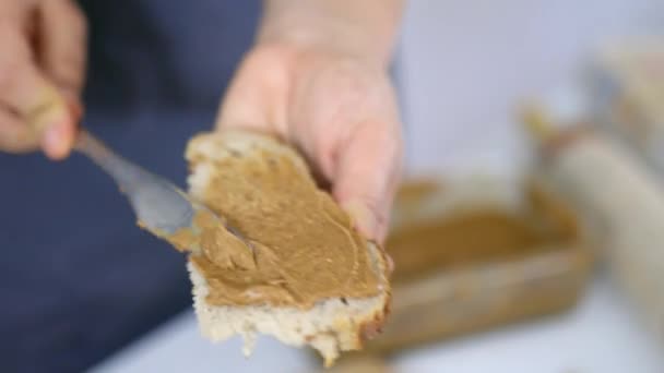 Mãos femininas espalhando manteiga de amendoim em uma fatia de pão — Vídeo de Stock
