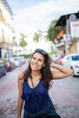 Güzel esmer kadın gülümsüyor ve tropik bir sokakta duruyor.