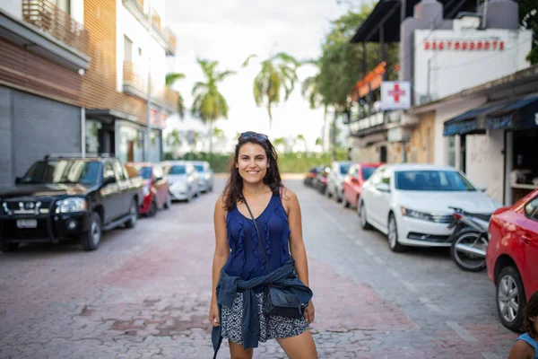 Güzel esmer kadın gülümsüyor ve tropik bir sokakta duruyor.