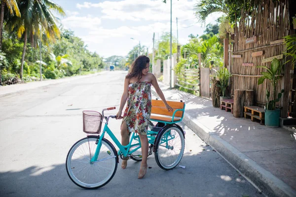 Elbise giyen ve üç tekerlekli bisiklet süren güzel bir kadın.