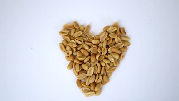 Small pile of peanuts in a heart shape on a white table — Stock Video