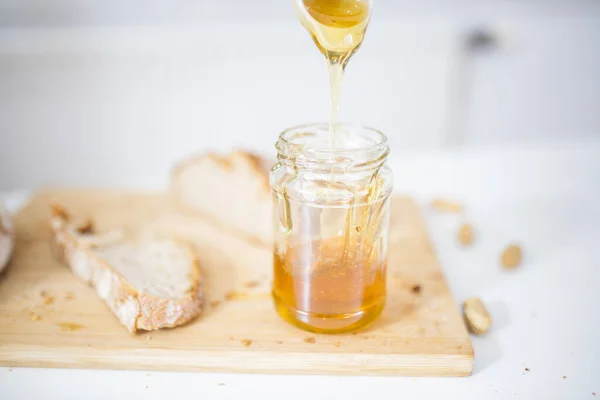 Frasco de mel e uma fatia de pão em uma tábua de madeira — Fotografia de Stock