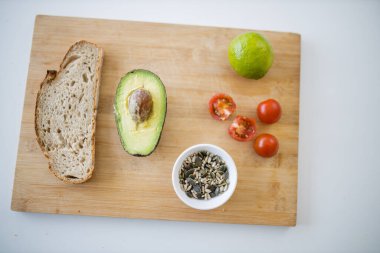 Dilimlenmiş ekmek, ikiye bölünmüş avokado, tahtanın üzerinde tohumlar ve domatesler.