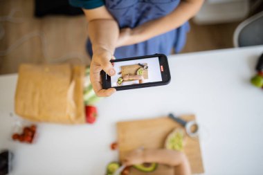 Akıllı telefonlu bir kadın, avokado kesen küçük bir kızı kaydediyor.