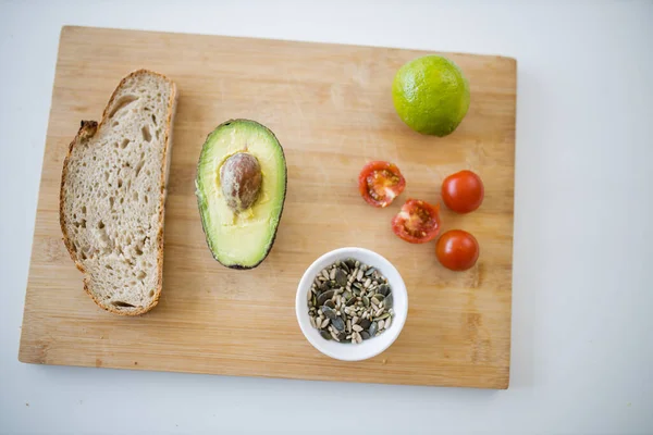 Dilimlenmiş ekmek, ikiye bölünmüş avokado, tahtanın üzerinde tohumlar ve domatesler.