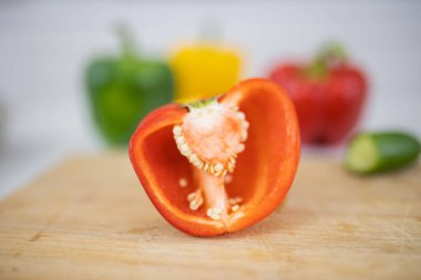 Arka planda sebzeler olan kesme tahtasında yarım kırmızı dolma biber.