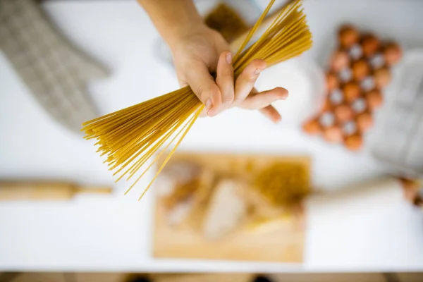 Mão feminina segurando espaguete não cozido acima dos ingredientes em uma mesa — Fotografia de Stock