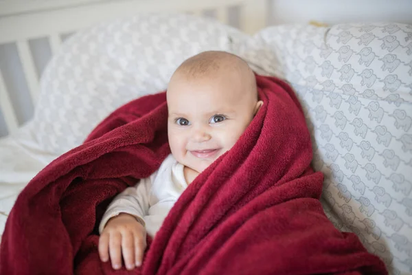 एक लाल कंबल से ढके हुए और बिस्तर पर पड़े हुए खुश बच्चे — स्टॉक फ़ोटो, इमेज