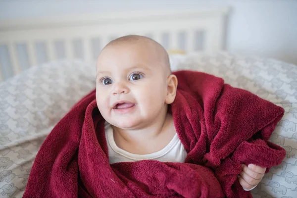 Счастливый ребенок, покрытый красным одеялом и лежащий на кровати — стоковое фото