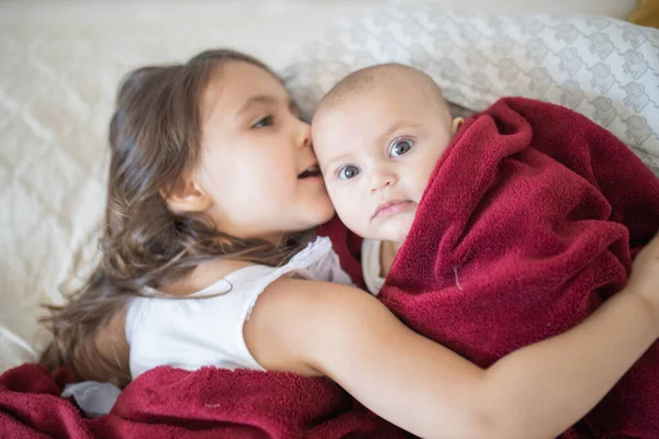 Schattig klein meisje en baby bedekt met een rode deken — Stockfoto