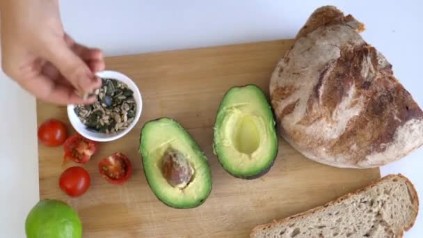 Kézzel szedett magok egy vágódeszkáról szeletelt kenyérrel és avokádóval — Stock videók