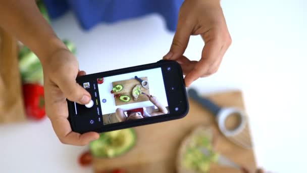 Vrouwelijke handen met een smartphone opnemen van een klein meisje snijden van een avocado — Stockvideo