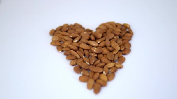 Pequeño montón de almendras en forma de corazón sobre una mesa blanca — Vídeos de Stock