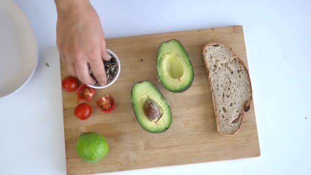 Recoger las semillas a mano de una tabla de cortar con pan en rodajas y aguacates — Vídeos de Stock