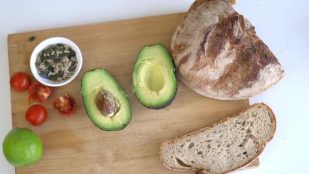 Skåret brød, avocado skåret i halve, frø og tomater på skærebrættet – Stock-video