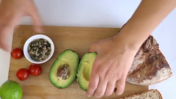 Hand pflückt eine Avocado von einem Schneidebrett mit Scheibenbrot und Samen — Stockvideo