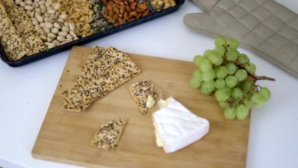 Manos femeninas recogiendo una uva de una tabla de cortar con pan crujiente y queso — Vídeos de Stock