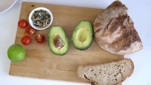 Recoger las semillas a mano de una tabla de cortar con pan en rodajas y aguacates — Vídeos de Stock