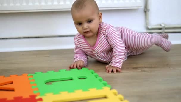 Bedårande baby liggande på trägolvet och leka med en färgglad matta — Stockvideo