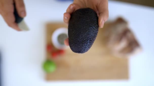 Ручной разрез авокадо пополам выше доски с нарезанным хлебом и помидорами — стоковое видео