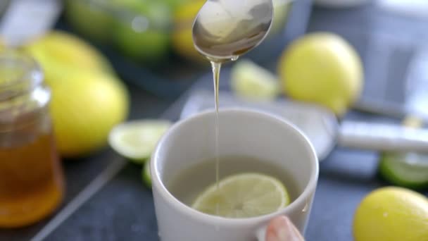 Mão feminina derramando mel e mexendo uma xícara de chá de limão — Vídeo de Stock