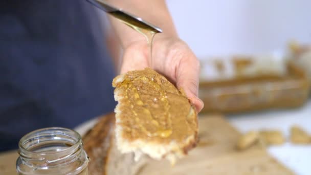 Mãos femininas espalhando mel em uma fatia de pão com manteiga de amendoim — Vídeo de Stock
