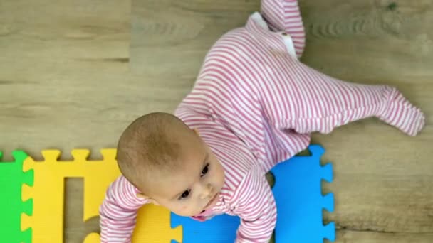 Αξιολάτρευτο μωρό ξαπλωμένο στο ξύλινο πάτωμα και παίζοντας με ένα πολύχρωμο χαλάκι — Αρχείο Βίντεο
