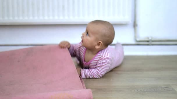 Glad baby liggande på trägolvet och bita en rosa matta — Stockvideo