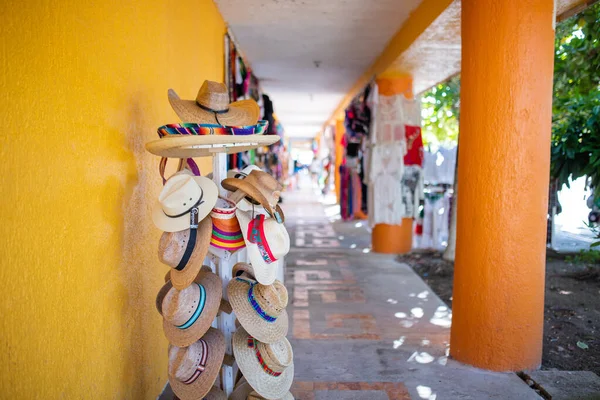 Straw hats hanging from a hat rack next to an orange wall