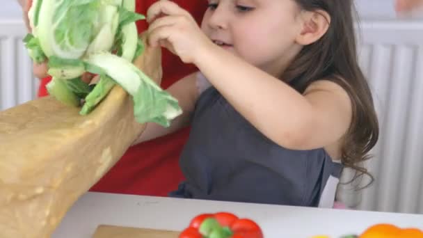 Ragazzina felice a un tavolo che tira fuori verdure da una borsa — Video Stock