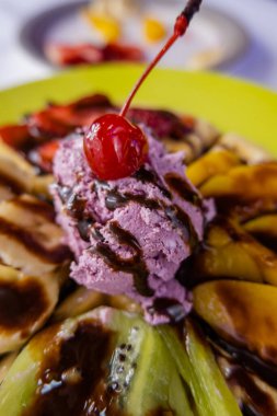 Çikolata şurubuyla süslenmiş meyveli dondurma ve kiraz.