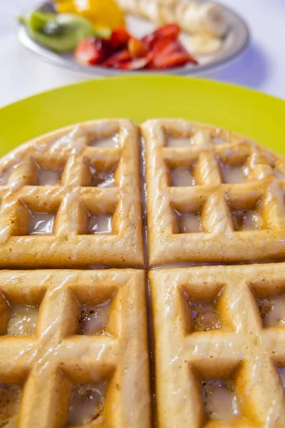 Gofre esmaltado en un plato amarillo con rodajas de fruta como fondo — Foto de Stock