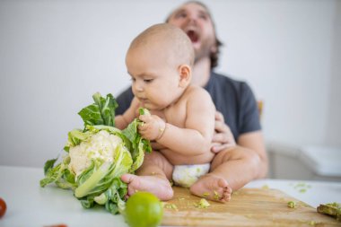Baba gülüyor ve küçük kızını masanın üstünde tutuyor.