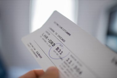 Arka planda pencere olan uçak bileti tutan bir erkek.