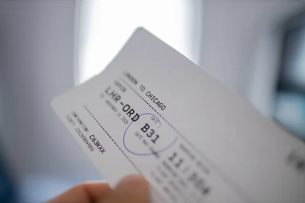 Male hand holding airplane ticket with a window as background