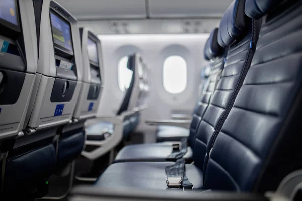 Empty dark blue seats with screens in the back inside an airplane