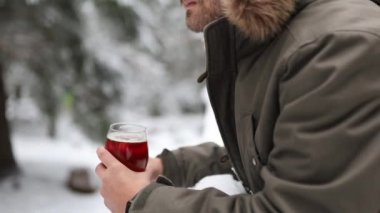 Arka planda karlı bir orman olan tırabzanlara yaslanan ve içen bir adam.