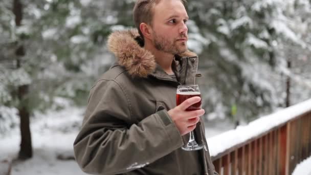 Homme buvant une boisson rouge avec une forêt enneigée comme arrière-plan — Video