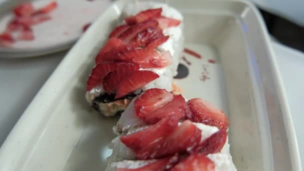 Rollos de sushi en un plato blanco con rodajas de fresa en la parte superior — Vídeo de stock