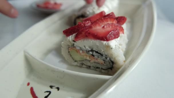 Manos poniendo rodajas de fresa en rollos de sushi encima de un plato blanco — Vídeo de stock