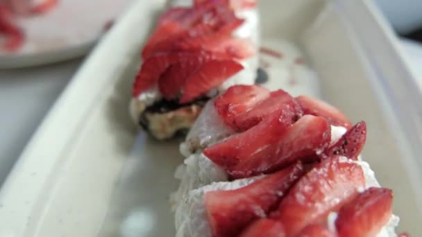 Tangan menempatkan strawberry irisan pada gulungan sushi di atas piring putih — Stok Video